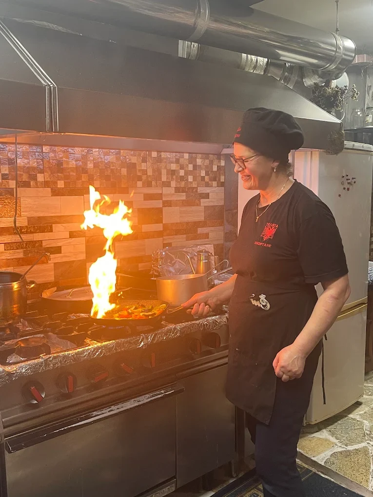 A cook preparing food in a pan at the Tradita kitchen stove.